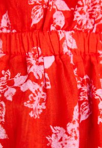 Czerwona tkanina z kwiecistym wzorem w jasnym różu, z marszczoną strukturą, tworzącą miękki, falujący wygląd. Odpowiednia do projektowania odzieży.