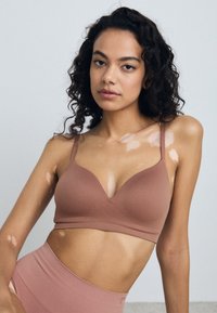 Soutien-gorge marron sans couture avec un décolleté en V, fines bretelles réglables et une texture de tissu lisse, associé à un bas taille haute assorti.