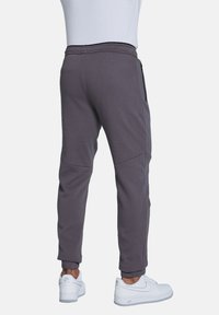Grey joggers with a tapered design, elastic waistband, and zippered pockets. Made of soft fabric, featuring ribbed cuffs and seamless side panels.