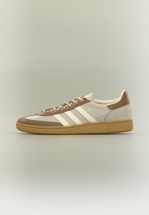 Baskets basses Adidas Spezial avec panneaux en cuir beige, marron clair et blanc, trois bandes blanches, semelle en gomme et lacets beiges.