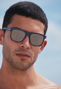 Crne pravokutne sunčane naočale sa zrcalnim staklima, glatkim plastičnim okvirom i metalnim detaljima na krunicama.