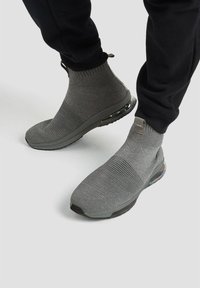Szare sneakersy przypominające skarpetki, z górą z teksturowanej tkaniny, wzorzystym detalem i wyściółką na podeszwie z widoczną jednostką powietrzną.