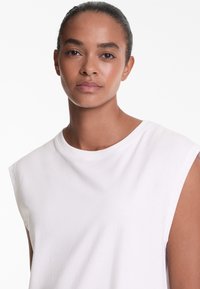 White sleeveless top with a rounded neckline, made of soft, smooth fabric. Minimalist design with no visible patterns or accents.
