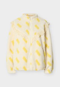 Κρεμ ζακέτα από φλις με κίτρινα ορθογώνια σχέδια, δαντέλα κατά μήκος του στήθους και των ώμων, εμπρόσθιο φερμουάρ και τσέπες με φερμουάρ στις πλευρές.