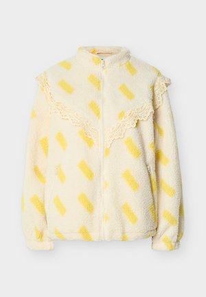 Κρεμ ζακέτα από φλις με κίτρινα ορθογώνια σχέδια, δαντέλα κατά μήκος του στήθους και των ώμων, εμπρόσθιο φερμουάρ και τσέπες με φερμουάρ στις πλευρές.