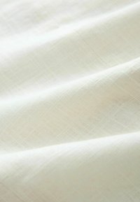 Lichtcrème stof met een subtiel textuurpatroon, voorzien van een fijne weving en een zachte afwerking, wat zorgt voor een delicate, luchtige uitstraling.