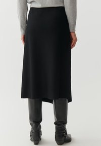 Zwarte midi-rok van een zacht materiaal, met een rechte snit en een subtiele high-low zoom. Gepaarde met glanzende zwarte kniehoge laarzen.