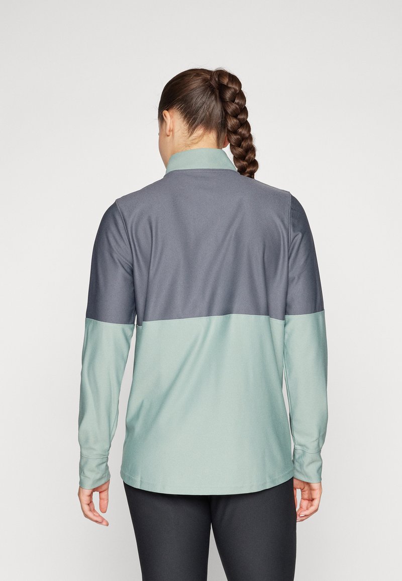 Maglietta atletica a maniche lunghe con design a blocchi di colore, presentante sezioni di grigio scuro e verde menta chiaro, con colletto e tessuto morbido e testurizzato.