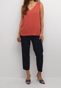 Coral sleeveless top with a V-neck, paired with navy tapered pants and blue high-heeled shoes. Simple design, smooth texture, and casual fit.
