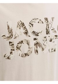 Λευκό βαμβακερό μπλουζάκι με την επιγραφή "JACK & JONES" σε μεγάλα γράμματα γεμάτα με μοτίβο φύλλου φοίνικα σε αποχρώσεις απαλού πράσινου και μπεζ.