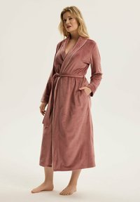 Różowy szlafrok z weluru z długimi rękawami, z wiązaniem w talii i kieszeniami po bokach. Posiada kołnierz szalowy i kontrastowe lamówki wzdłuż brzegów.