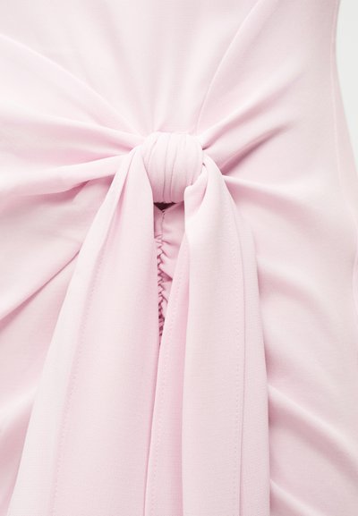 Μαλακό ροζ ύφασμα δεμένο σε κεντρικό κόμπο με πτυχώσεις που συγκεντρώνονται από κάτω, δημιουργώντας ρέουσες πτυχές.