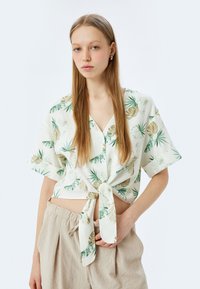 Korte mouwen, cropped shirt van lichte stof met een bladerenpatroon in groen en beige, met een strikdetail aan de voorkant.
