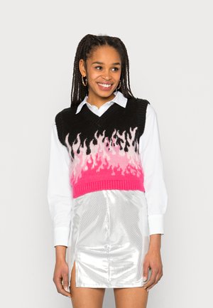 Top cropped preto com padrão de chamas em rosa e branco, combinado com uma saia mini prateada brilhante e uma camisa branca de botões.