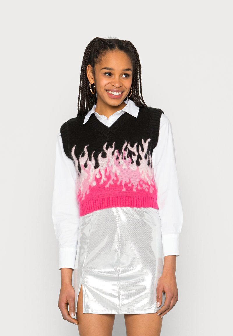 Top cropped preto com padrão de chamas em rosa e branco, combinado com uma saia mini prateada brilhante e uma camisa branca de botões.