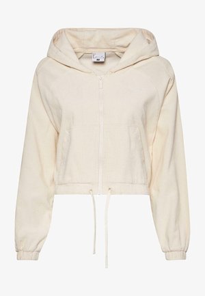 Zrezaná mikina s kapucňou v svetlej béžovej farbe vyrobená z kordu, s predným zipsom, šnúrkou na spodnom leme a elastickými manžetami. Na hrudi je jemné logo.