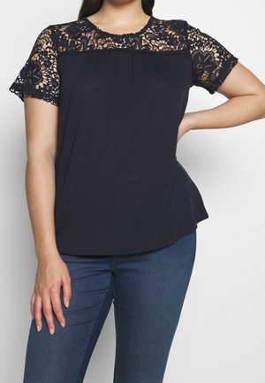 Granatowa bluzka z krótkimi koronkowymi rękawami, z kwiatowym wzorem na koronce i lekko marszczonym dekoltem. Gładki materiał.