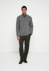 Γκρι πλεκτό πουλόβερ με γιακά, δύο κουμπιά και ριμπ μανσέτες, συνδυασμένο με χακί παντελόνια και σκούρα καφέ παπούτσια.