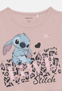 Różowa koszulka z krótkim rękawem z niebieską postacią z kreskówki "Stitch", z czarnymi i szarymi akcentami w leopardzi wzór oraz błyszczącym napisem "LOVE".