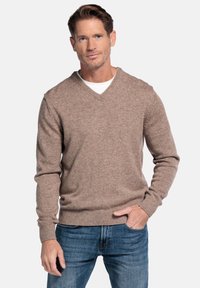 Brauner Wollpullover mit V-Ausschnitt, gerippten Bündchen und Saum, getragen über einem weißen Hemd, kombiniert mit blauen Jeans. Glatte Textur, lässiges Design.