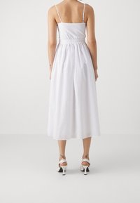 Vit midi-klänning med en åtsittande överdel, tunna axelband och elasticitet i midjan. Den texturerade tyget och den utsvängda kjolen har ett subtilt mönster.