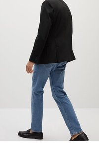 Musta räätälöity bleiseri, jossa on avonaiset läpät, yhdistettynä vaaleansinisiin farkkuihin ja mustiin loafereihin, luoden tyylikkään ja modernin ilmeen.