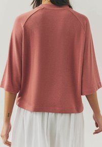 Haut à manches raglan en tissu doux et texturé de couleur rose poussiéreuse. Il présente un col rond et une coupe décontractée, avec un ourlet droit.