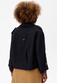 Czarna lniana marynarka o luźnym kroju, szerokich klapach i zapinanych na guziki mankietach. Posiada mały detal z logo na plecach.