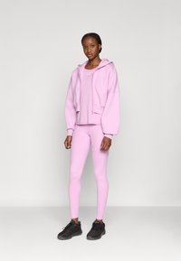 Ανοιχτό ροζ cropped φούτερ με κορδόνι, συνδυάζεται με ταιριαστό εφαρμοστό τοπ και κολάν. Μαύρα αθλητικά παπούτσια ολοκληρώνουν το σύνολο.