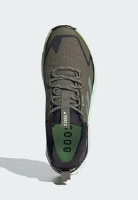Zapatilla deportiva verde y negra con parte superior de malla, diseño texturizado, acentos reflectantes y contrafuerte acolchado. Incluye cordones y logo.