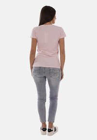 Donna in piedi di spalle che indossa una maglietta rosa chiaro, jeans skinny grigi sbiaditi e sneaker bianche con dettagli neri.