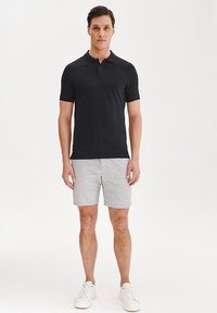 Czarny polo, szare szorty o teksturowanym wzorze i białe sneakersy. Prosty sportowy design, krótkie rękawy i klasyczny kołnierzyk.