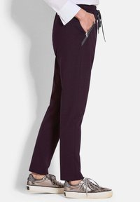 Donkerpaarse joggingbroek met een elastische tailleband, voorzien van zijzakken met rits en gecombineerd met metallic schoenen. Glad textuur van de stof.