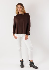 Maglione marrone a maniche lunghe, taglio morbido e ampio, abbinato a pantaloni bianchi aderenti e stivaletti neri alla caviglia con cerniere. Design semplice e classico.