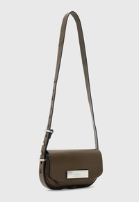 Ruskea nahkainen olkalaukku, jossa on tyylikäs suorakulmainen muoto, säädettävä olkahihna, hopeiset yksityiskohdat ja sileä pinta. Sisältää metallisen koristeen.