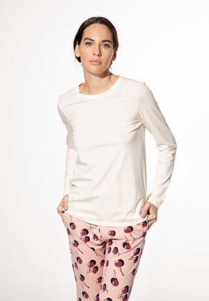 Long-sleeve cream top with a round neck, paired with light pink pants featuring a cherry print. Smooth texture, fitted design, minimal seams.