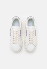 Zapatillas blancas y lavanda con superficie texturizada, cordones beige y suela de goma suave. Logo redondo en la plantilla.