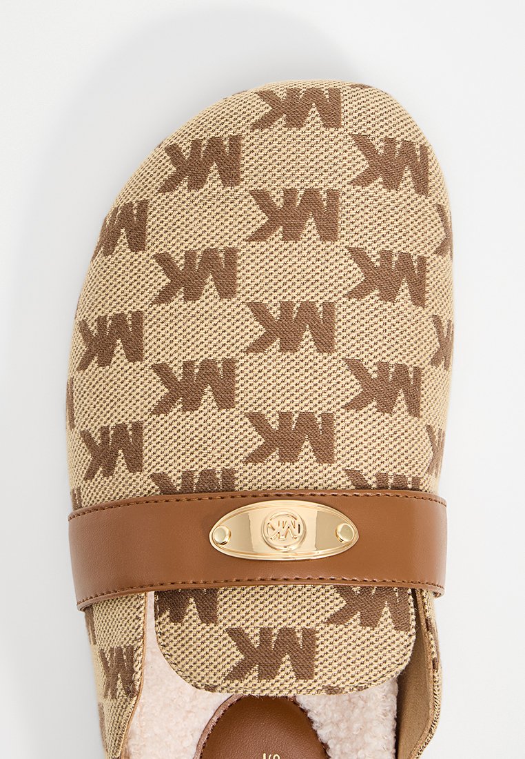 Beige snörningslös sko med brunt "MK" mönster, guldfärgad logotypdetalj och brun läderrem, med en mjuk, plyschig foder.