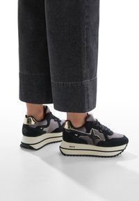 Sneakers con un mix di camoscio blu navy e accenti metallici, dotati di una spessa suola bianca e un design a stella sul lato. Finitura texturizzata e lacci.