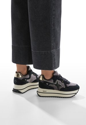Sneakers with a mix of navy suede and metallic accents, featuring a thick white sole and star design on the side. Textured finish and laces.