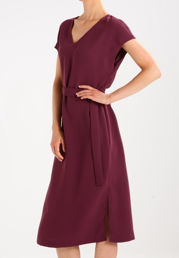 V-Ausschnitt, kurzärmliges Kleid aus tiefburgunderfarbenem Stoff, mit einem Bindegürtel und seitlichem Schlitz für zusätzliche Details, das eine fließende Silhouette präsentiert.
