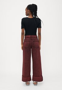 Top corto a maniche corte nero a coste abbinato a jeans bordeaux a vita alta e gamba ampia con orli sfilacciati e tasche posteriori. Orecchini a cerchio in argento.