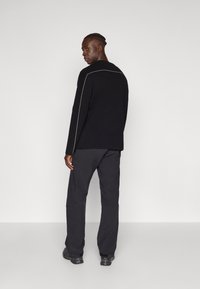 Sweater preto com costura branca ao longo das costuras dos ombros, combinado com calças escuras e largas. O tecido parece suave com um acabamento texturizado.