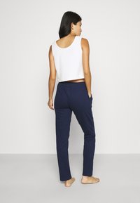 Witte cropped tank top en marineblauwe broek met elastische taille, met zakken en een gladde textuur, gezien vanuit de achterkant.