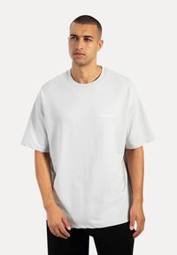 T-shirt oversized grigio chiaro con collo rotondo, maniche corte e logo sul petto. Tessuto morbido, design minimalista e vestibilità rilassata.