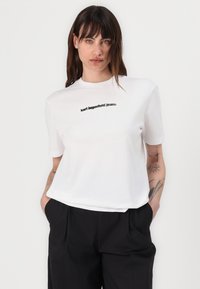 White cotton t-shirt with short sleeves, featuring a black printed logo "karl lagerfeld jeans" across the chest, smooth texture, relaxed fit.