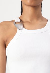 Witte geribbelde tanktop met een gebogen grijze metalen accent op de band. De stof heeft een gladde textuur en een aansluitend ontwerp.