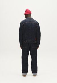Temno modra denim jakna in ujemajoče hlače z sproščenim krojem. Rdeča pletena kapa. Oprema vključuje gumbe in žepke; subtilno kontrastno šivanje.