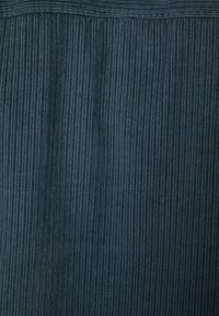 Mörkblått tyg med vertikal ribbad textur, som har växlande tunna och breda ränder, och en slät ytkvalitet.