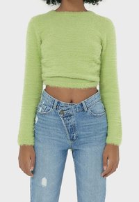 Sweater court à manches longues vert clair en matériau doux et pelucheux. Associé à un jean taille haute bleu clair déchiré avec une fermeture à boutons.